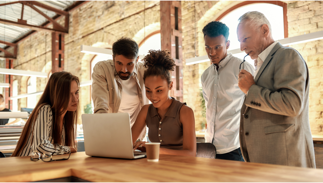 a group of people huddle around a laptop in a warmly lit board room