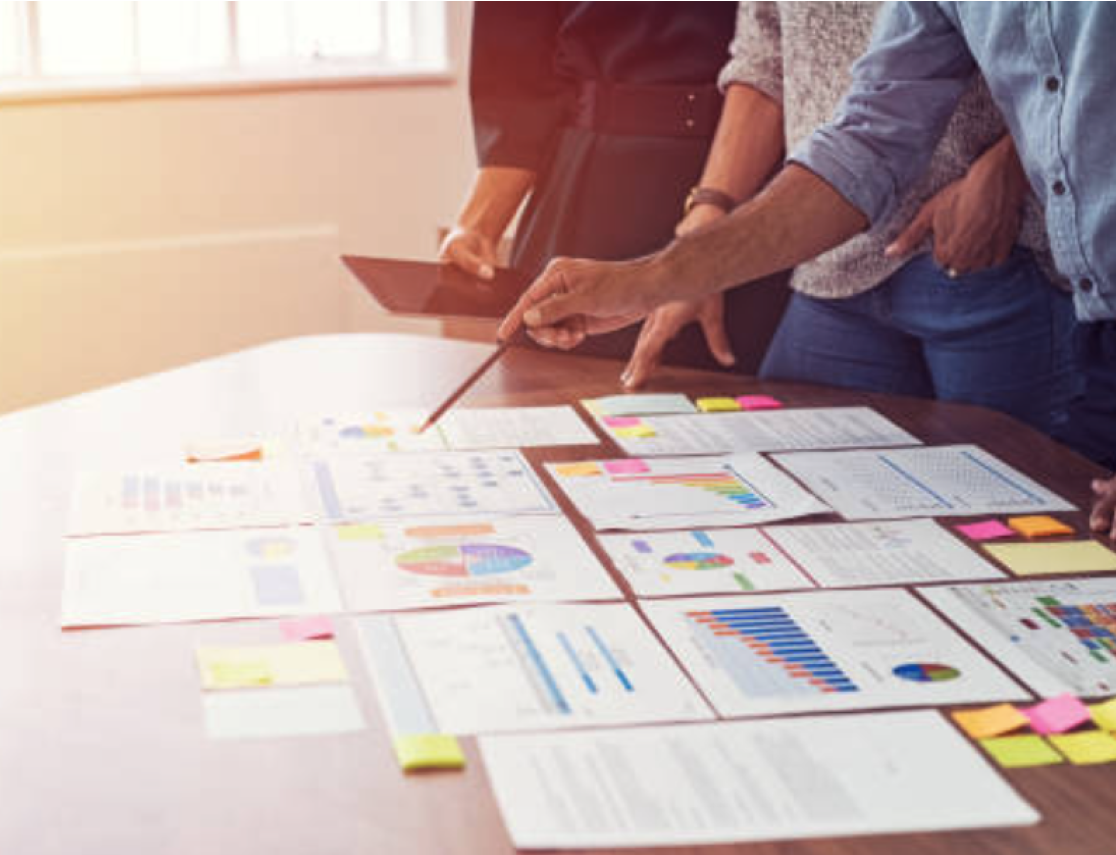 three people point to a collection of printed charts and graphs, analyzing the data