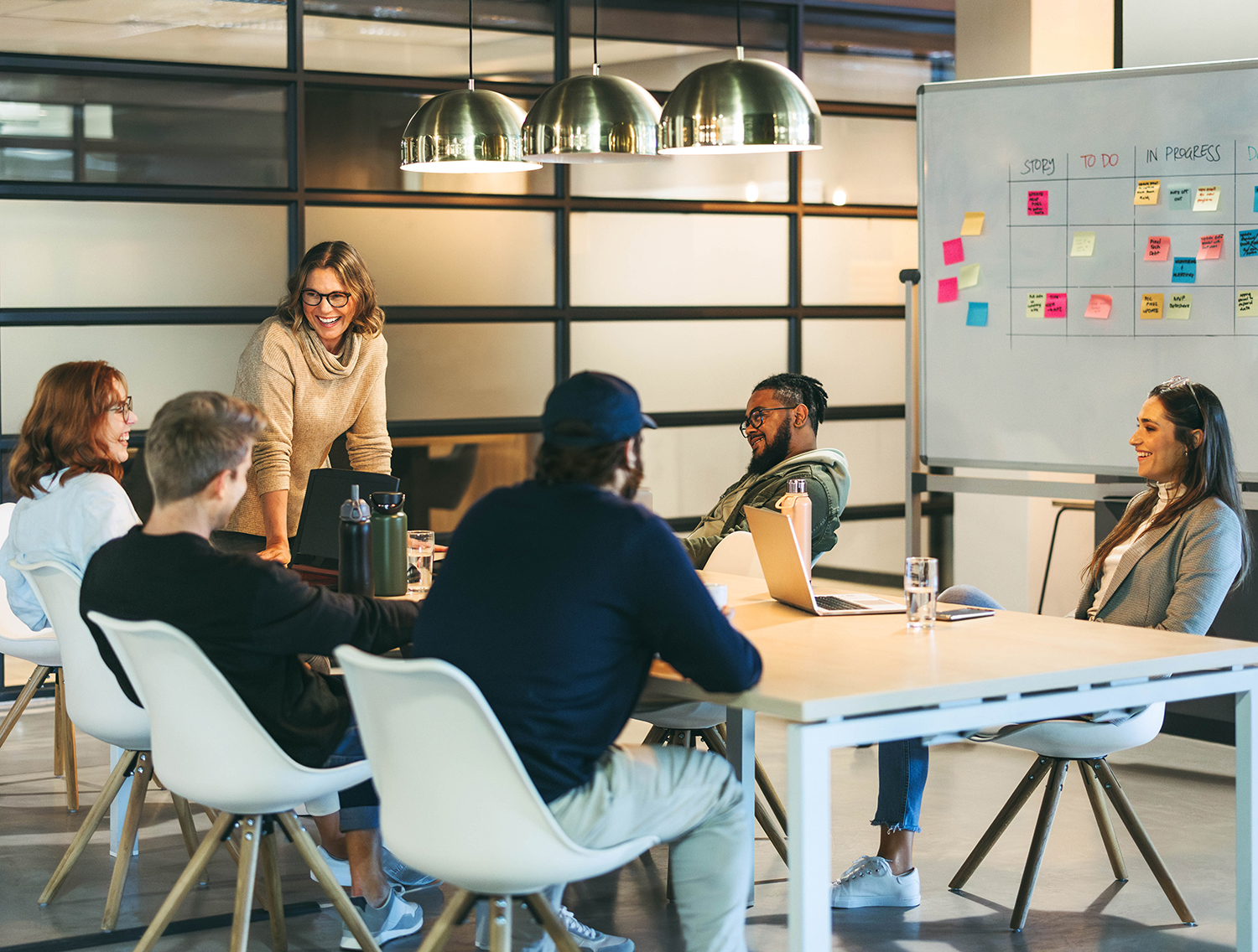 Business people in a boardroom engage in a creative discussion, exchanging ideas with a confident leader facilitating the meeting. The happy team represents successful collaboration and a modern tech company's productive work environment.