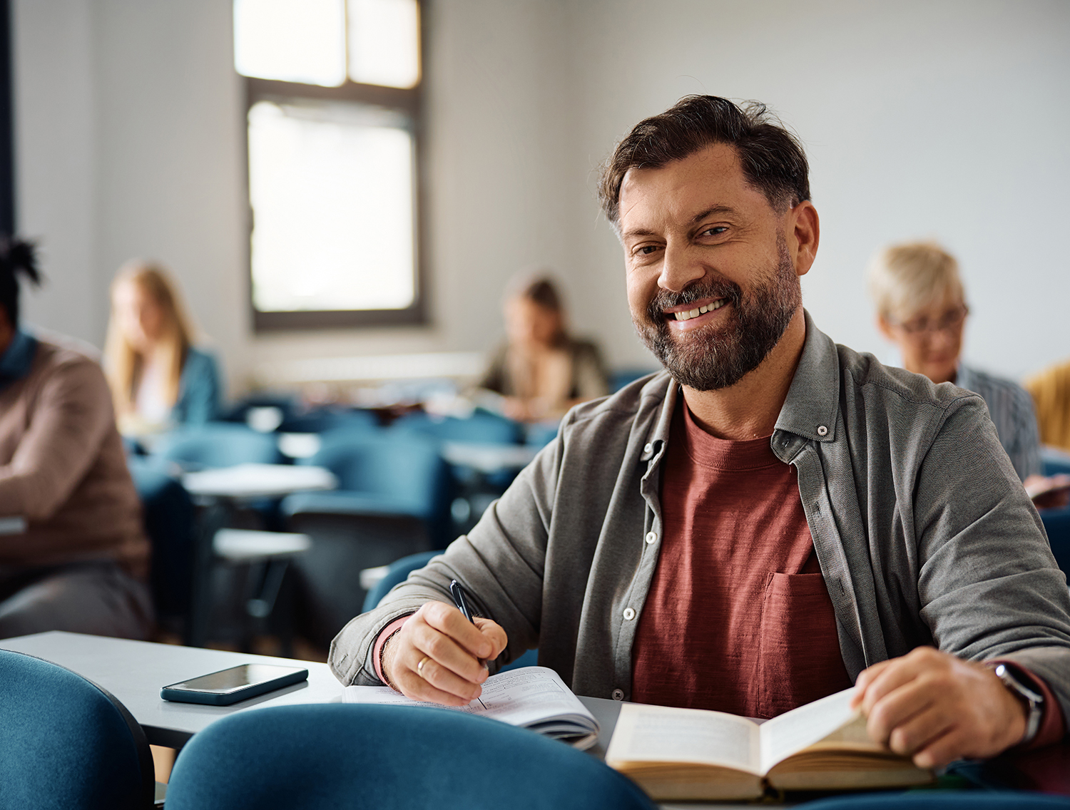 Happy mature student taking learning during a class in lecture hall and looking at camera.