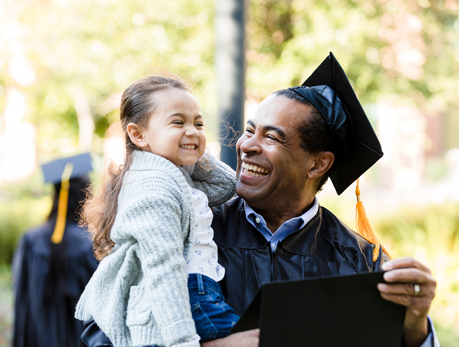 The little preschool age girl makes a silly face. Her mature adult grandfather smiles and laughs. He has just graduated.