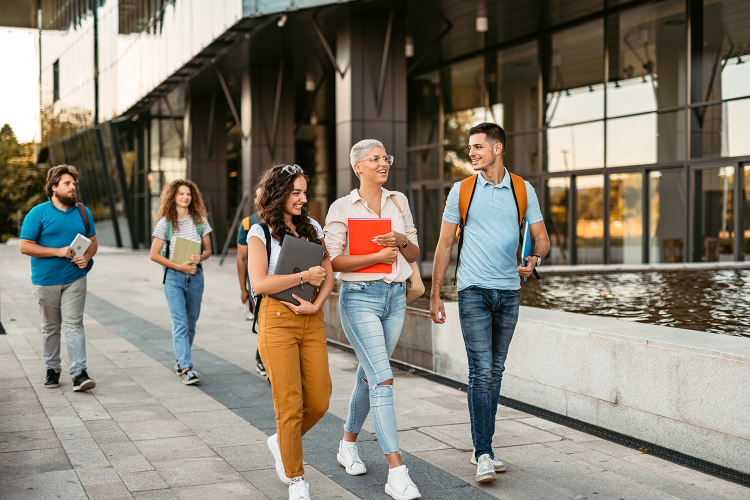 Group of friends walking on the university campus, holding books and notebooks.